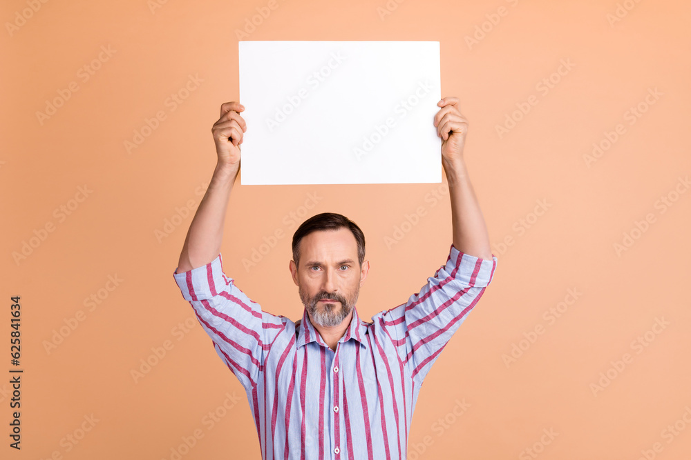 Photo of serious confident man with white gray beard dressed striped shirt hold placard over head isolated on beige color background Photo of serious confident man with white gray beard dressed striped shirt hold placard over head isolated on beige color background