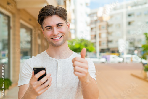 Young handsome man using mobile phone while doing thumbs up