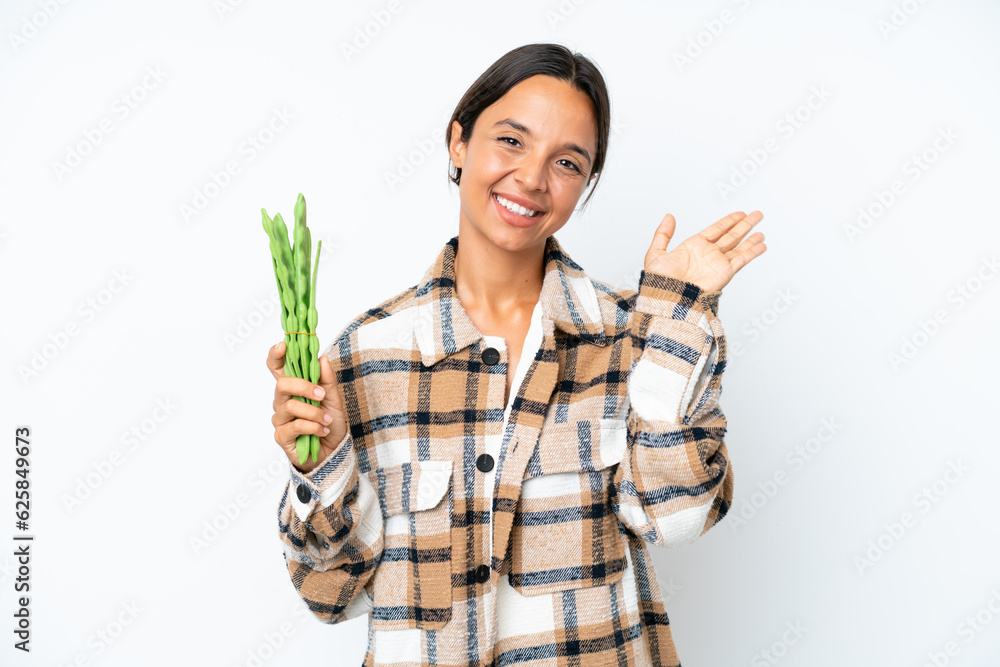 Young hispanic woman holding a green beans isolated on white background saluting with hand with happy expression Young hispanic woman holding a green beans isolated on white background saluting with hand with happy expression