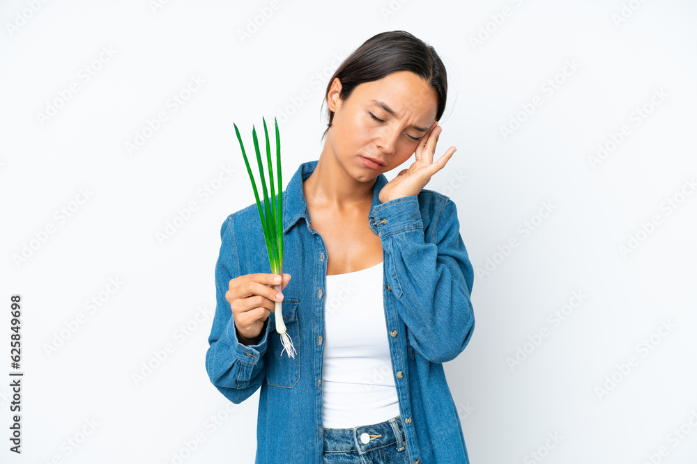 Young hispanic woman holding chive isolated on white background with headache Young hispanic woman holding chive isolated on white background with headache