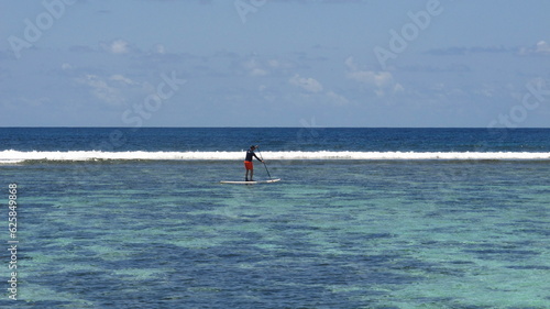 A figure sup sailing in the beach clear water