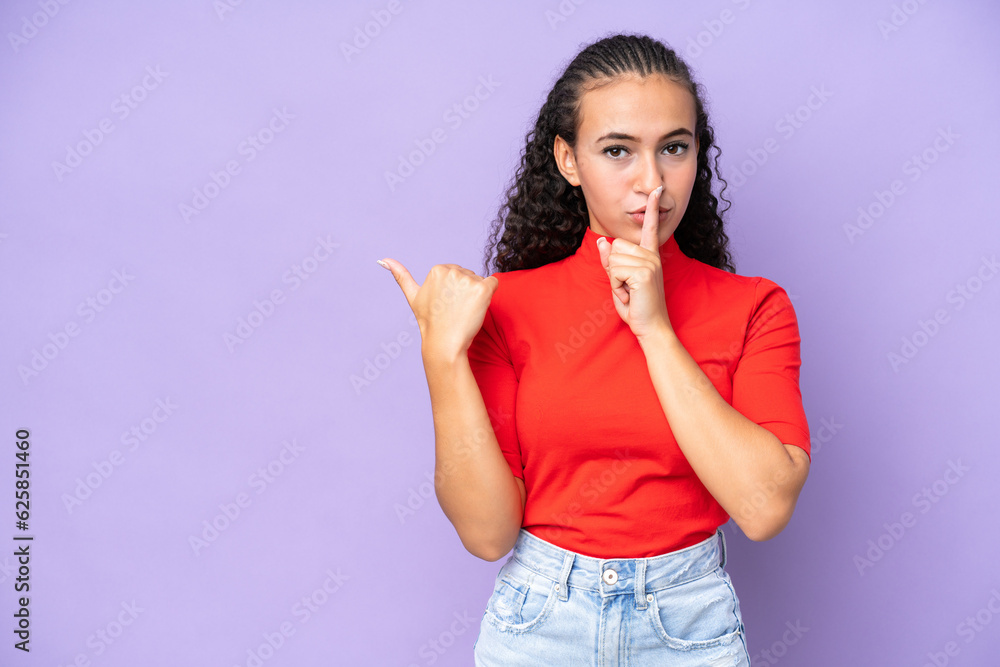 Young woman isolated on purple background pointing to the side and doing silence gesture Young woman isolated on purple background pointing to the side and doing silence gesture