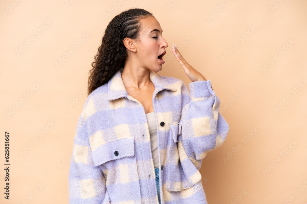 Young woman isolated on beige background yawning and covering wide open mouth with hand Young woman isolated on beige background yawning and covering wide open mouth with hand