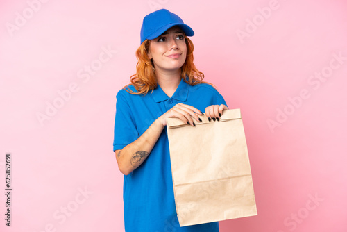 Young caucasian woman taking a bag of takeaway food isolated on pink background having doubts and thinking