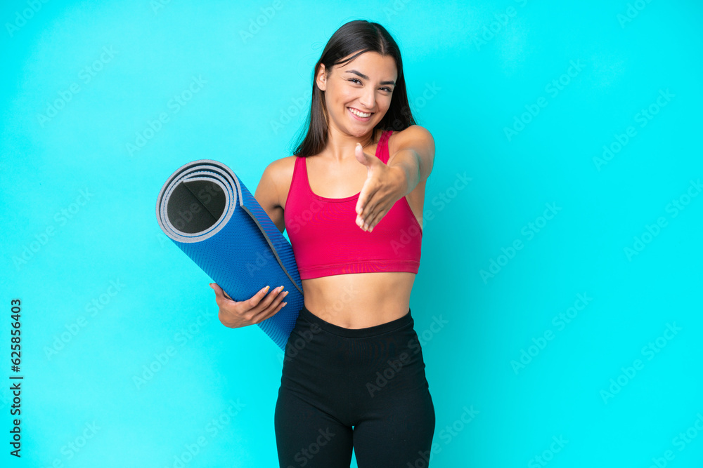 Young sport caucasian woman going to yoga classes while holding a mat isolated on blue background shaking hands for closing a good deal Young sport caucasian woman going to yoga classes while holding a mat isolated on blue background shaking hands for closing a good deal