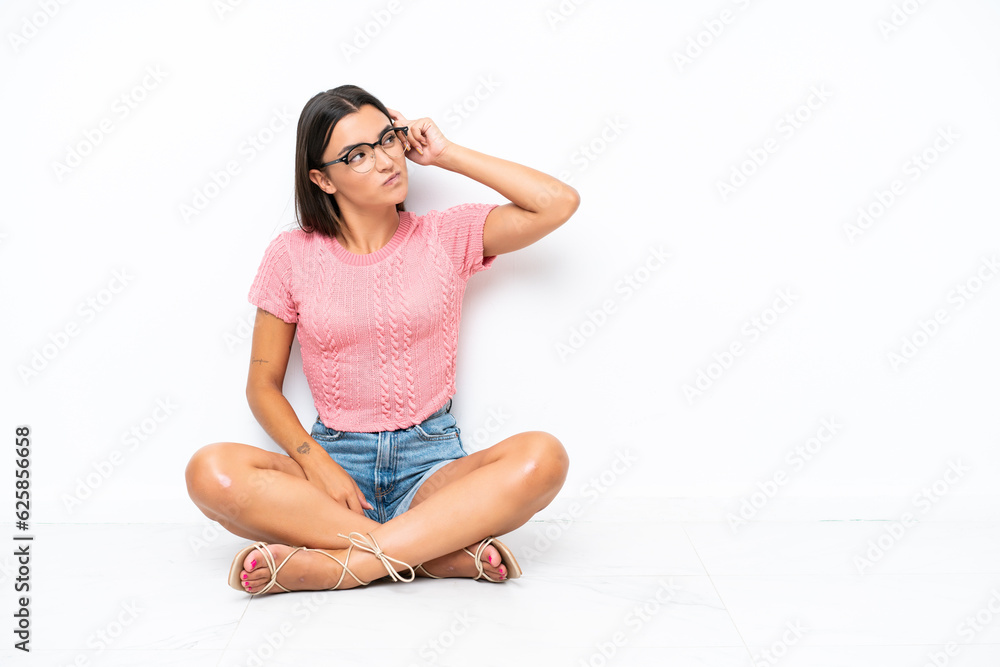 Young caucasian woman sitting on the floor isolated on white background having doubts and with confuse face expression Young caucasian woman sitting on the floor isolated on white background having doubts and with confuse face expression