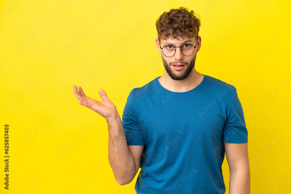 Young handsome caucasian man isolated on yellow background making doubts gesture