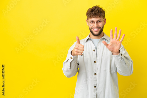 Young handsome caucasian man isolated on yellow background counting six with fingers