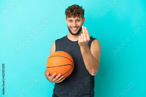 Handsome young man playing basketball isolated on blue background making money gesture © luismolinero