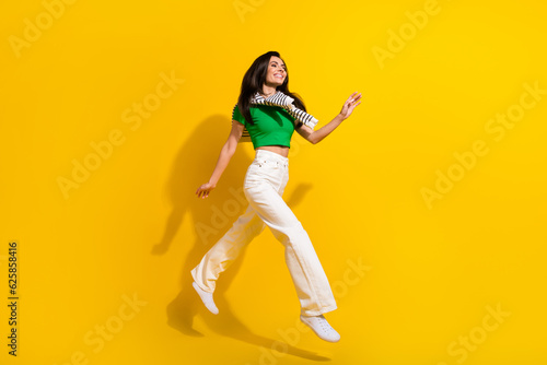 Full length photo of cute pretty girl dressed green t-shirt running fast jumping high isolated yellow color background