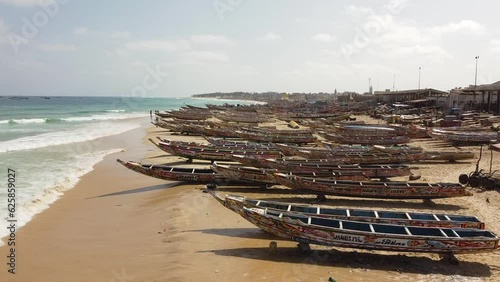Endless colorful fishing boats sit on the sandy beach pointed to the ocean. The wooden boats are traditional here in the fishing village of Kayar (Senegal), where many dangerous migrations begin.