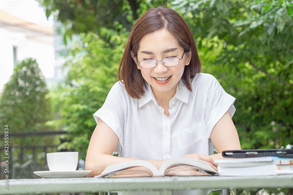 Fototapeta premium Asian middle aged woman in glasses reading a book in backyard