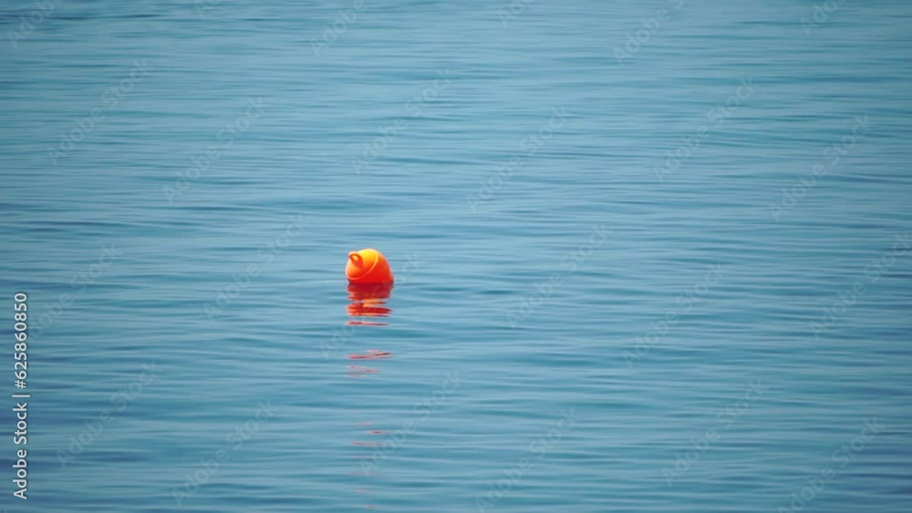 Orange buoy floating on the surface of the sea waves, concept of human life safety. Orange safety buoys on a rope floating in the sea on a sunny day, close up. Fencing of the swimming area on beach. Orange buoy floating on the surface of the sea waves, concept of human life safety. Orange safety buoys on a rope floating in the sea on a sunny day, close up. Fencing of the swimming area on beach.