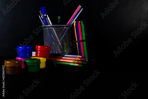 Front shot of oil color bottles with crayons, pencil colors, and pens in a stand against black background. photo