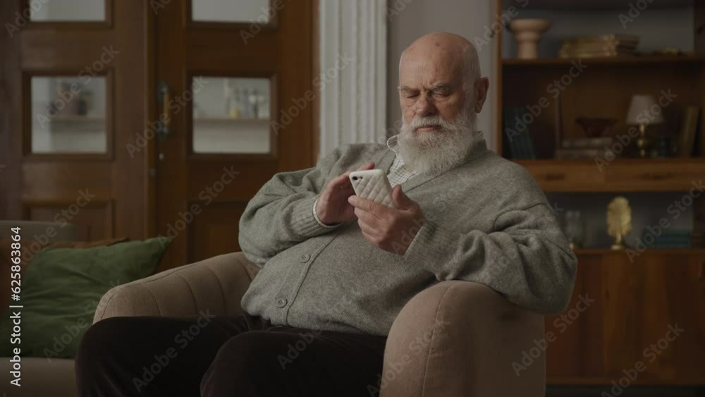 Elderly Man Browsing on Smartphone in Armchair Elderly Man Browsing on Smartphone in Armchair