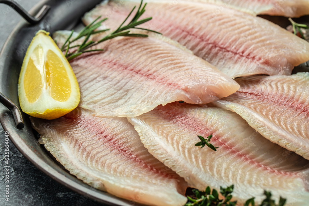 raw Tilapia fish, skinless meat with lemon and spices on a dark background. raw Tilapia fish, skinless meat with lemon and spices on a dark background.