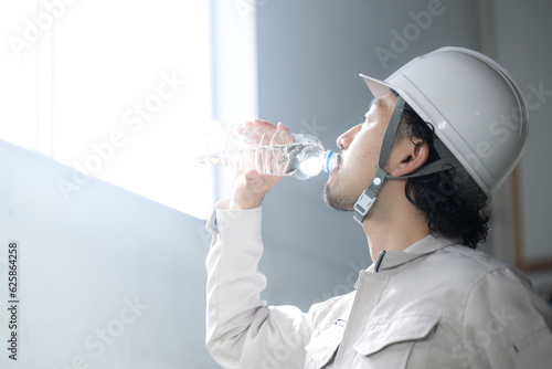 作業着姿で水分補給する作業員の男性　熱中症予防もご安全に photo
