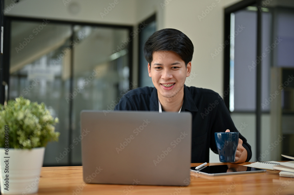 A happy Asian businessman working on his project on his laptop at his desk. A happy Asian businessman working on his project on his laptop at his desk.
