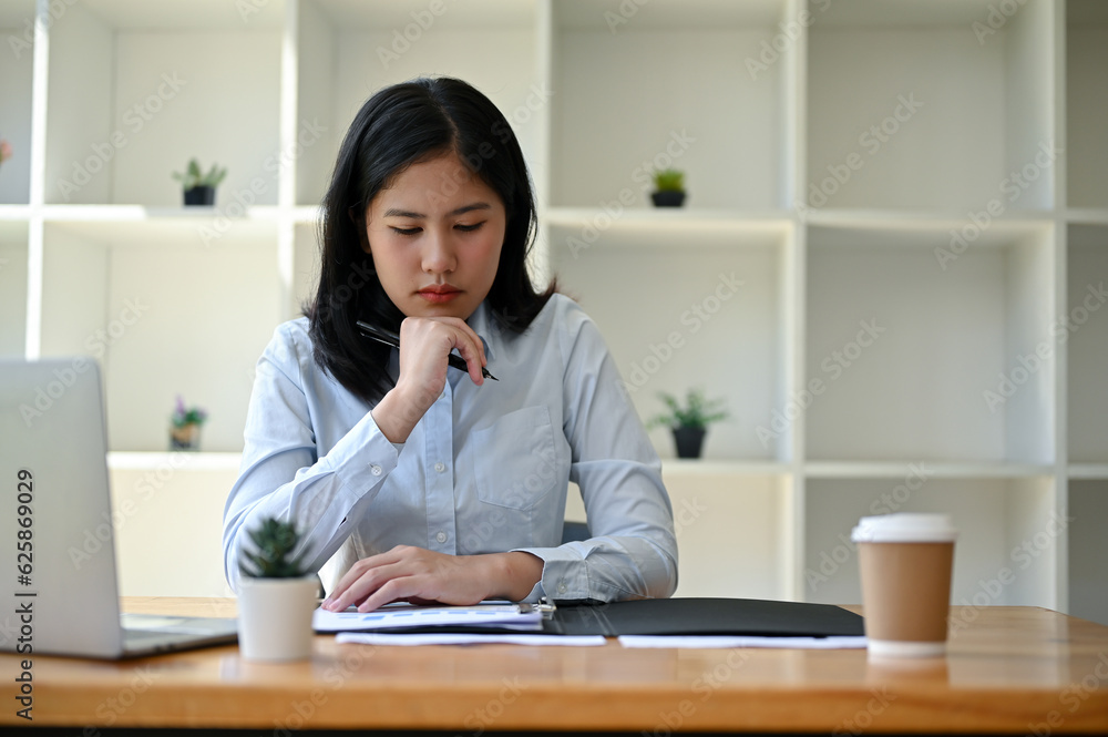 A serious and thoughtful Asian businesswoman planning her project and working on her tasks A serious and thoughtful Asian businesswoman planning her project and working on her tasks