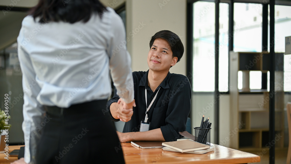 A handsome Asian office worker shaking hands with a new female colleague in the office. A handsome Asian office worker shaking hands with a new female colleague in the office.