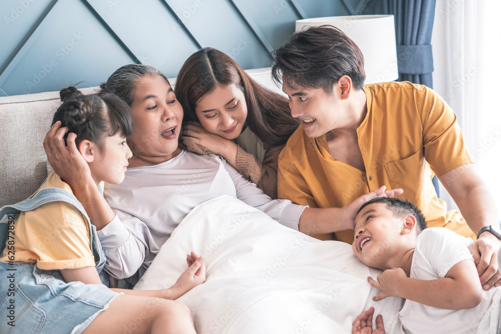 Fototapeta premium family of five embracing, a grandmother with a daughter, a son and a granddaughter, a granddaughter sitting in the house hugging grandma on the bed.