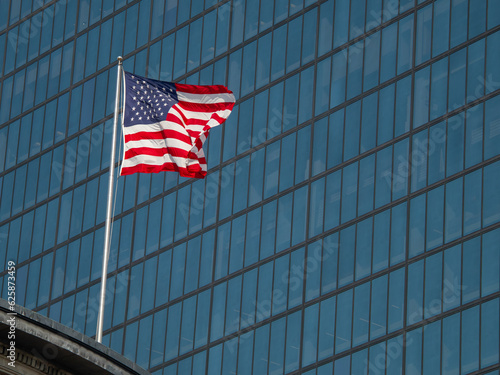 Flags of the United States waving in the wind with modern office building in the background.