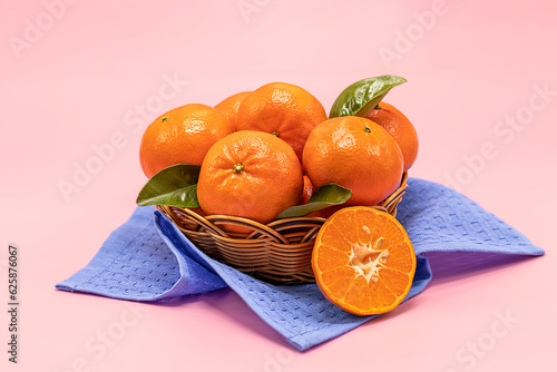 Fresh tangerines in a basket on a pink background.