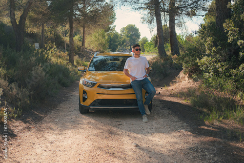 Latin man poses with a yellow car in a road
