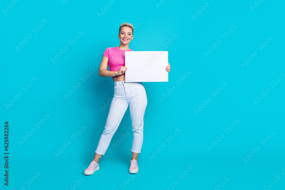 Full length photo of adorable lovely woman dressed pants sneakers falling hold white placard empty space isolated on blue color background