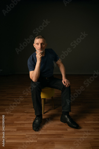 a handsome elderly man with a gray beard sits and looks into the camera, studio photo, selective focus