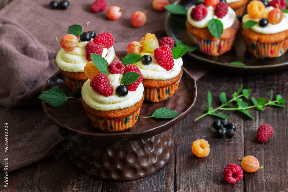 Cupcakes with butter cream and raspberry curd, decorated with berries on a wooden surface.