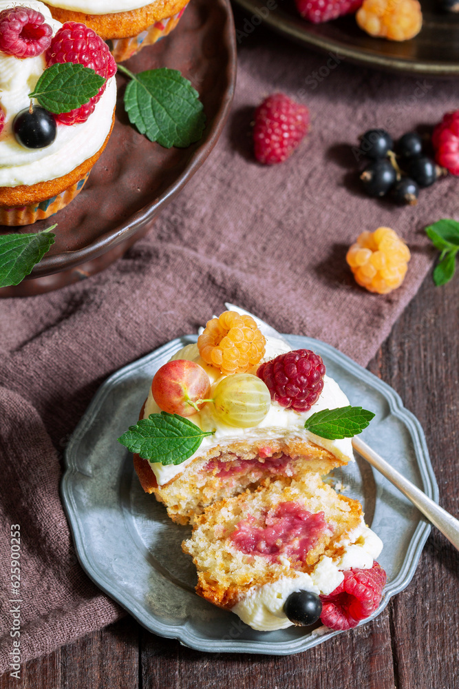 Cupcakes with butter cream and raspberry curd, decorated with berries on a wooden surface.