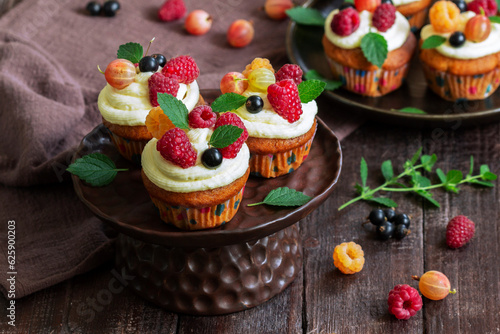 Obraz na płótnie Cupcakes with butter cream and raspberry curd, decorated with berries on a wooden surface. w salonie