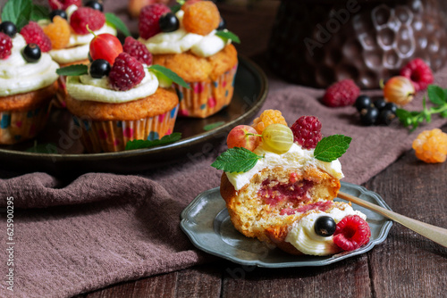 Obraz na płótnie Cupcakes with butter cream and raspberry curd, decorated with berries on a wooden surface. w salonie
