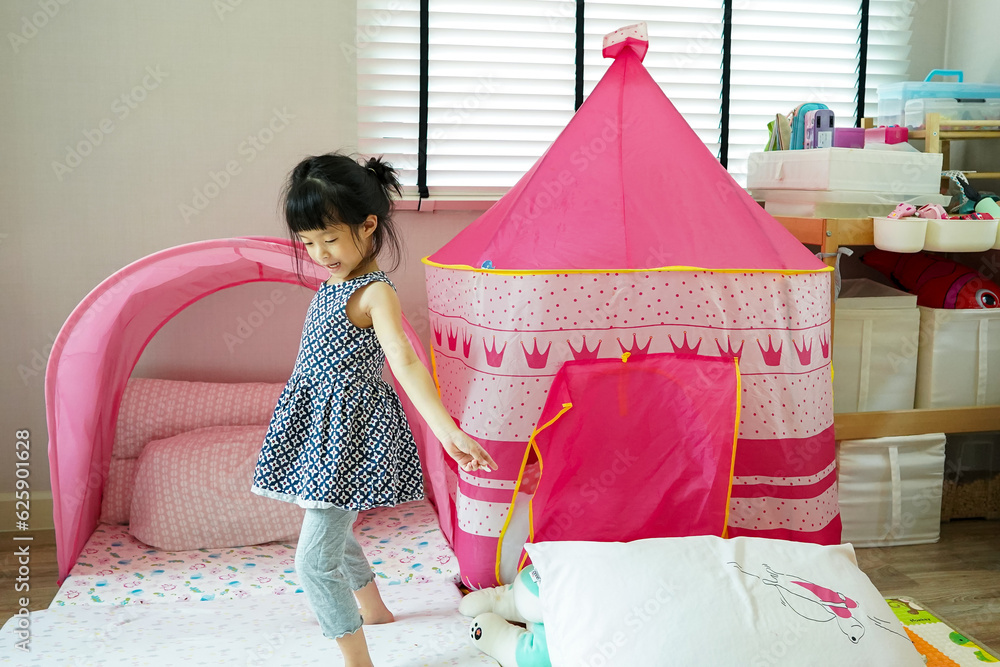 Naklejka premium Little girl be cheeky ,look so funny and playful in her play room at home.Home child room decoration design.