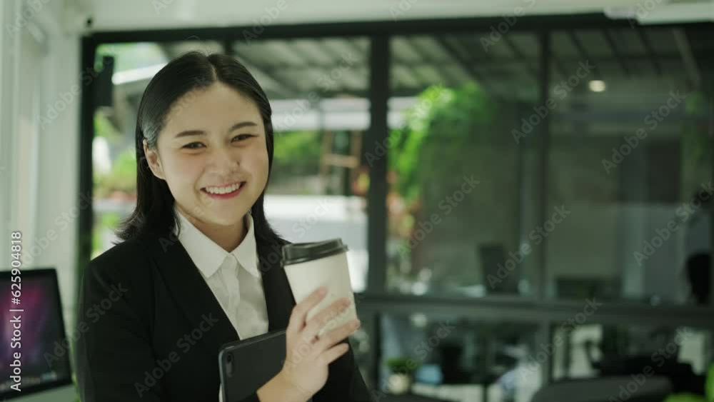 Shot in slow motion of confident female manager holding paper cup of coffee and smiling to camera Shot in slow motion of confident female manager holding paper cup of coffee and smiling to camera