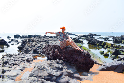 Stone sea coast. Boulders on the seashore. Girl sits on a big stone in the sea