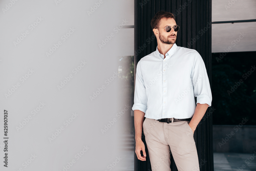 Handsome confident stylish hipster lambersexual model. Modern man dressed in white shirt and trousers. Fashion male posing in the street urban background in sunglasses. Outdoors Handsome confident stylish hipster lambersexual model. Modern man dressed in white shirt and trousers. Fashion male posing in the street urban background in sunglasses. Outdoors