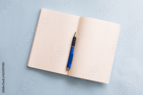 Top view of open empty notes and blue pen on blue background. School or office background ideas.