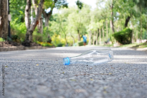 An empty of drinking plastic bottle littering on the ground floor in plubic park road with blurred street  background