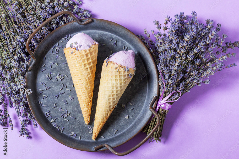 Two lavender ice creams in waffle cones on a tin tray and bouquets of dry lavender on a lilac background.