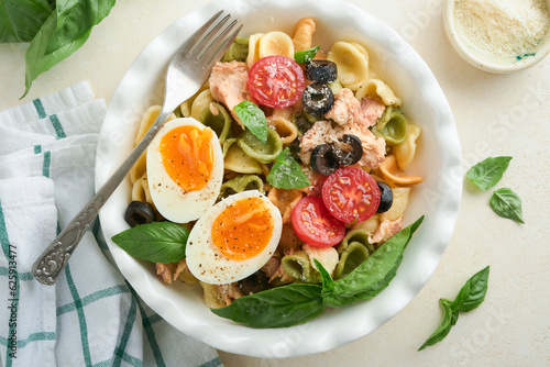 Italian pasta salad. Orecchiette pasta with tuna, tomato cherry, olive, basil and parmesan cheese in plate on grey stone or concrete background. Traditional Italian cuisine. Flat lay. Copy space.