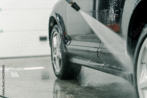 Close-up of a male car wash employee washing the sills of the rims of a black luxury car with a high-pressure washer 