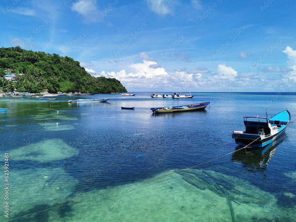 Banda Island, Indonesia - May 20, 2022. Beautiful sea and beach view with turquoise sea color, white clouds, blue sky, trees and bright sunshine and sailing ships.