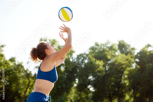Young woman playing beach volleyball on sunny day, serving ball with hands. Outdoors training on fresh air. Concept of sport, active and healthy lifestyle, hobby, summertime, ad © master1305