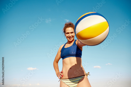 Young smiling woman holding volleyball ball, posing over blue sky background. Outdoor summer training. Concept of sport, active and healthy lifestyle, hobby, summertime, ad #625944644