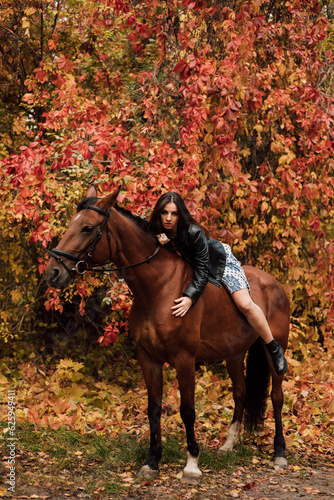 Young beautiful woman posing on a horse in the forest. Autumn nature