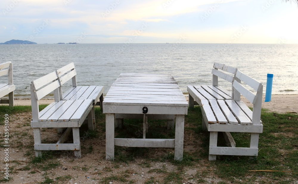 Set white painted table and benches on sand and sea, sky background with sunlight, white cloud in sky. Set white painted table and benches on sand and sea, sky background with sunlight, white cloud in sky.