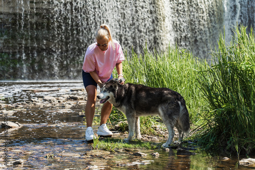 A woman walks with a husky dog ​​at the Jägala waterfall in summer. © Dmitri