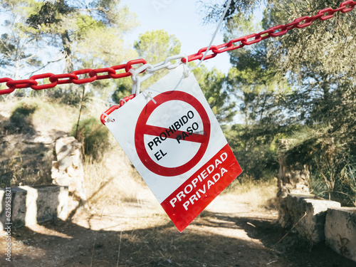 Red warning sign hangs on tree, barring access to private property in spanish language - translated as No trespassing, private property. Ideal for safety communication projects. photo